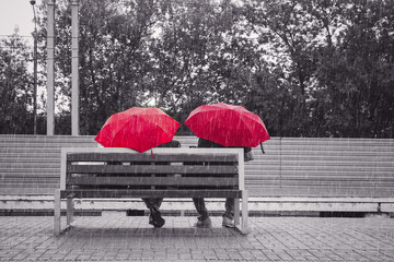 Couple in love sitting on the bench on a platform under umbrellas in the rain