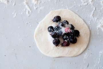 On the table is rolled out circle of dough with filling in the middle, the berries of amelanchier. Cooking dumplings with berries concept.