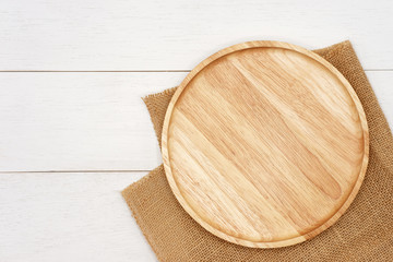 Empty round wooden plate with rustic brown burlap cloth on white wooden table. Top view image.
