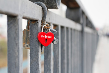 Red padlock in the form of heart and with the words "Me&you" hanging on fence