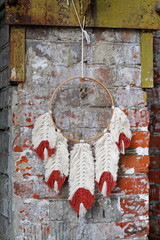 White-red macrame feathers  hang on round dreamcatcher against a brick wall.