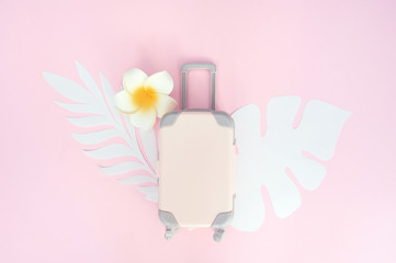 Pink travel suitcase on pink background with tropical leaves and white flower. Concept for travel. Flat lay exotic