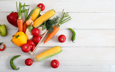 Useful vegetable set for a vegetarian in a box on wooden background top view. Corn, pepper, carrot, eggplant, tomato, onion and dill in the grocery basket.