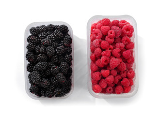 Raspberries and blackberries in trays top view on isolation