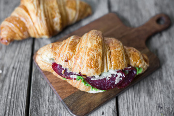 Croissant sandwich on the wooden table with salami, cheese and fresh salad food photography