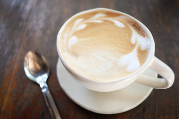 Latte coffee in the white cup on wooden foods table.