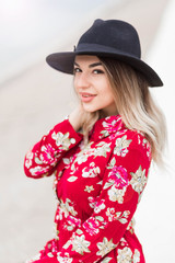 Beautiful girl in red dress and black hat poses for the camera