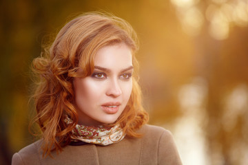 Naklejka premium Stylish woman in beige coat and gloves standing in autumn yellow park.