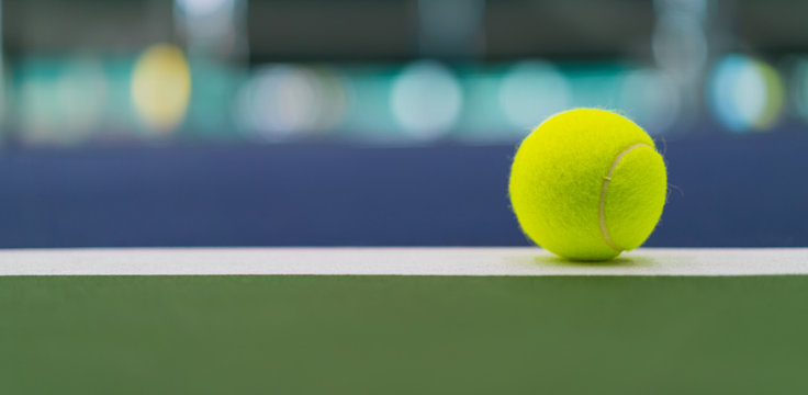 one new tennis ball on white line in blue and green hard court with beautiful bokeh, copy space on left