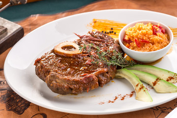 Prepared Osso buco Veal shank with avocado slices and rice on white plate on old map background