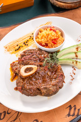 Prepared Osso buco Veal shank with avocado slices and rice on white plate on old map background