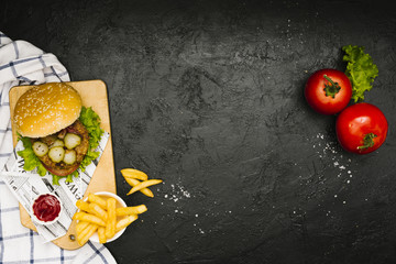 Flat-lay burger and fries on wooden board with copyspace