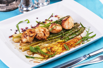  European recipe, Mediterranean dish. Caramelized asparagus with onion chips, rose petals, arugula and pieces of fried fish