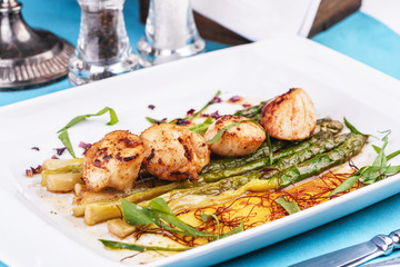  European recipe, Mediterranean dish. Caramelized asparagus with onion chips, rose petals, arugula and pieces of fried fish