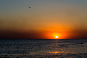 Airplane flying over the sea at the sunset