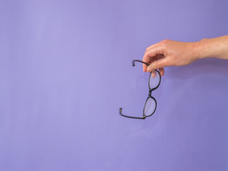 Hand with glasses on purple background with copy space