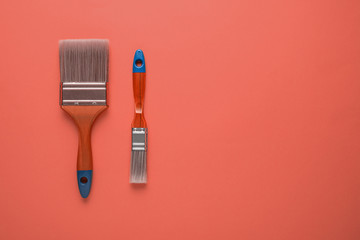 Two painting brushes on trendy background of live coral color with copy space