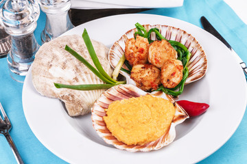 European recipe, Mediterranean dish. Baked mollusk in the oven under a cheese cap, served with crispy fish slices and greens, onions and red pepper according to a national recipe