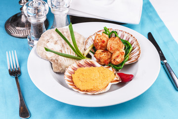European recipe, Mediterranean dish. Baked mollusk in the oven under a cheese cap, served with crispy fish slices and greens, onions and red pepper according to a national recipe