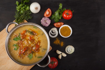 Red lentil soup with tomatoes, onions, garlic, herbs and spices in a metal pan on a black background. Copy spaes.