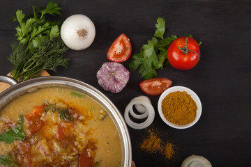 Red lentil soup with tomatoes, onions, garlic, herbs and spices in a metal pan on a black background.