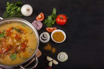 Asian red lentil soup with tomatoes, onions, garlic, herbs and spices in a metal pan on a black background. opy spaes.