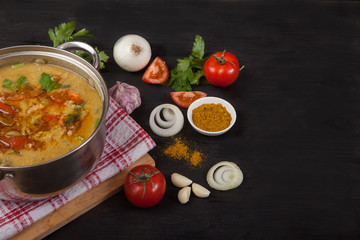 A red lentil soup casserole stands on a napkin on a black background. Near onion, garlic and spices. Copy spaes.
