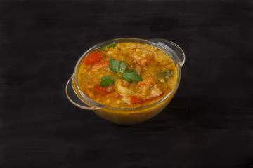 Red lentil soup in a glass bowl with spices, herbs, onion and garlic on a black background. Copy spaes.