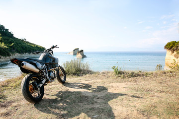A motorcycle on the sandy cliff on the blue sky and ocean view in distance.