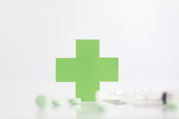 Green medical cross symbol and syringe with pill on white background