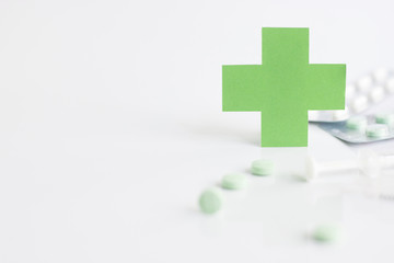 Obraz premium Green medical cross symbol and syringe with pill on white background
