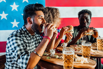 Leisure, eating, food and drinks, people and holidays concept - smiling friends having dinner and drinking beer  and eat burgers at restaurant or pub