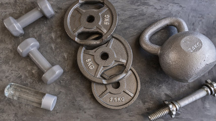 Obraz na płótnie Canvas Weight plates for barbell, grey dumbbells, kettlebell and water bottle in cement floor in gym. Equipment for weight training and building muscle. Concept for sport or workout