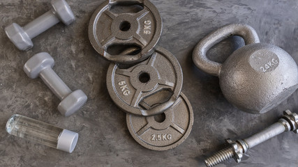 Weight plates for barbell, grey  dumbbells, kettlebell  and water bottle in cement floor in gym. Equipment  for weight training and  building muscle. Concept for sport or workout