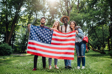 Group of mixed race college students holding an American flag on nature.