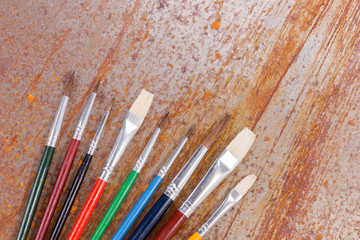 Row of colorful paint brushes are lying jumbled on the rusty background