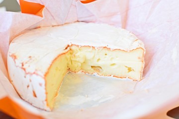 Top side view of a Camembert cheese in the open original paper package.