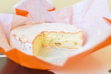 Side view of Camembert cheese in the open original paper package.