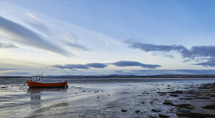 Sunset over a moored small boat  in the Montrose Basin on a winters day with the tide out.