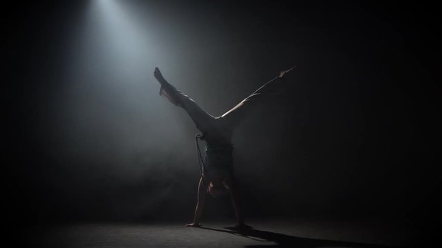 Curly maiden practicing capoeira in darkness against spotlight in studio.