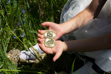 Bitcoins in children's hands. Children's hands hold gold bitcoins on the background of green grass.