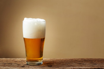 Glass beer on wooden table with cream wall background. copy space for design.
