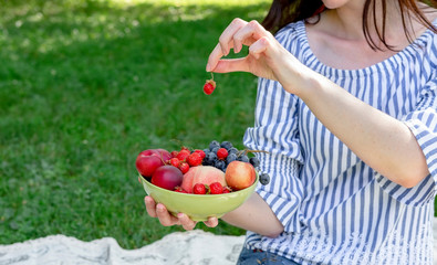  Young woman holds a bowl of fruit on a picnic.