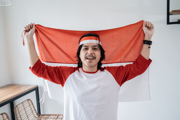 portrait of young asian male holding indonesian flag. patriotic nationalism concept