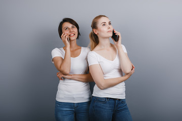 Two women  talking on mobile phone  against a grey studio background.- Image