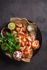 Raw prawns in a pan with ingredients for cooking on a dark background top view