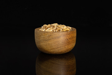 Lot of whole fresh beige dinkel wheat grain in a wooden bowl isolated on black glass