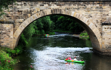 Fototapeta Ludzie w kajakach płyną rzeką pod starym mostem, spływ kajakowy. obraz