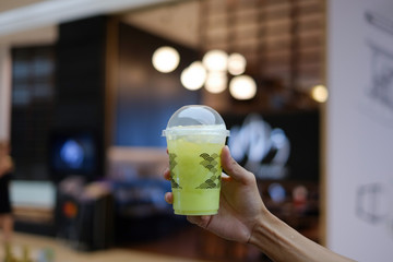 hand holding a plastic cup of fresh melon juice and bubble drinks , focus , bokeh background