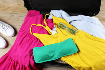 Open suitcase fully packed with folded women's clothing and accessories on the floor. Woman packing for tropical vacation concept. Female luggage w/ things. Background, close up, copy space, top view.